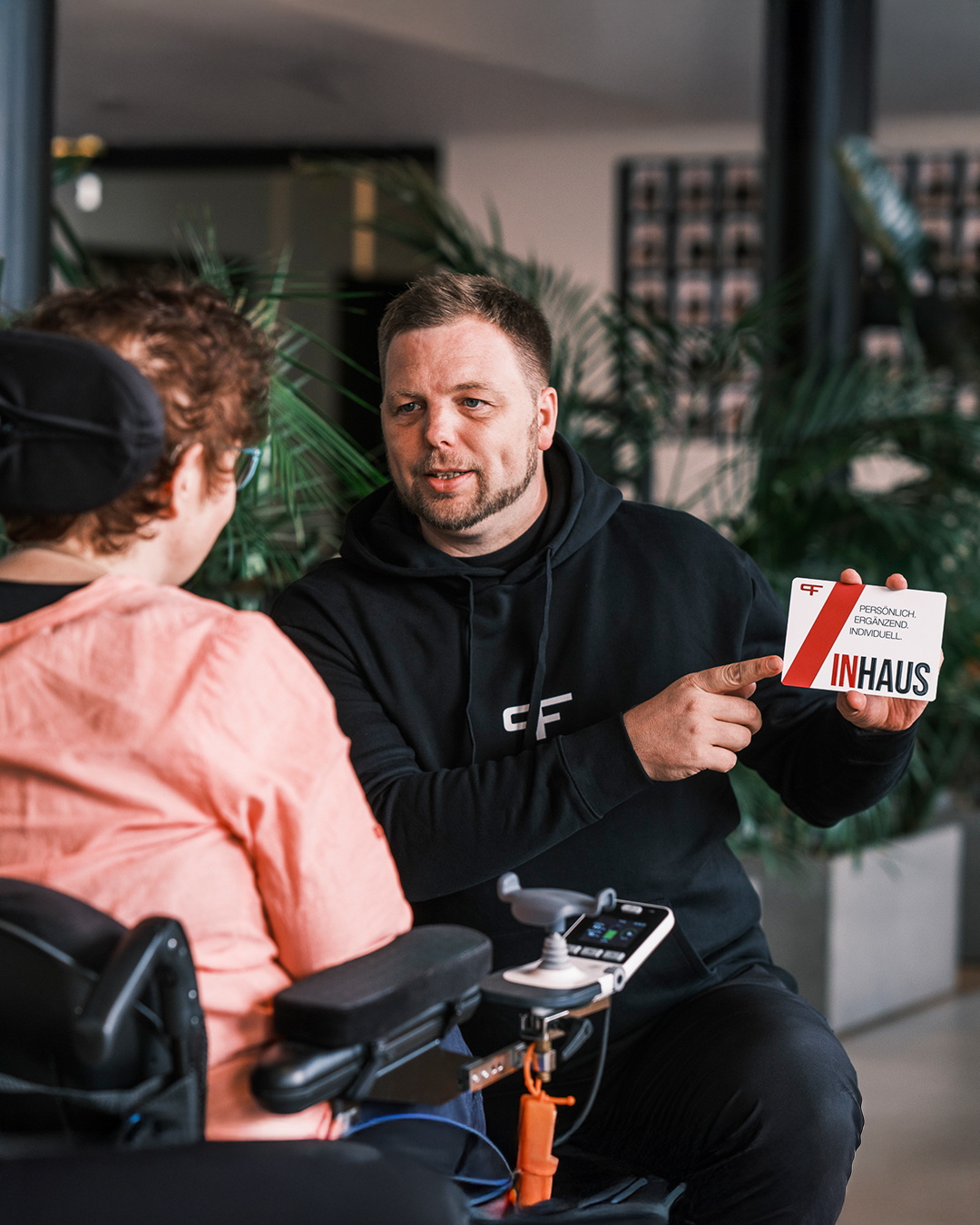 Ein Physiotherapeut erklärt einer Frau im Rollstuhl eine Informationskarte über ein Trainingskonzept